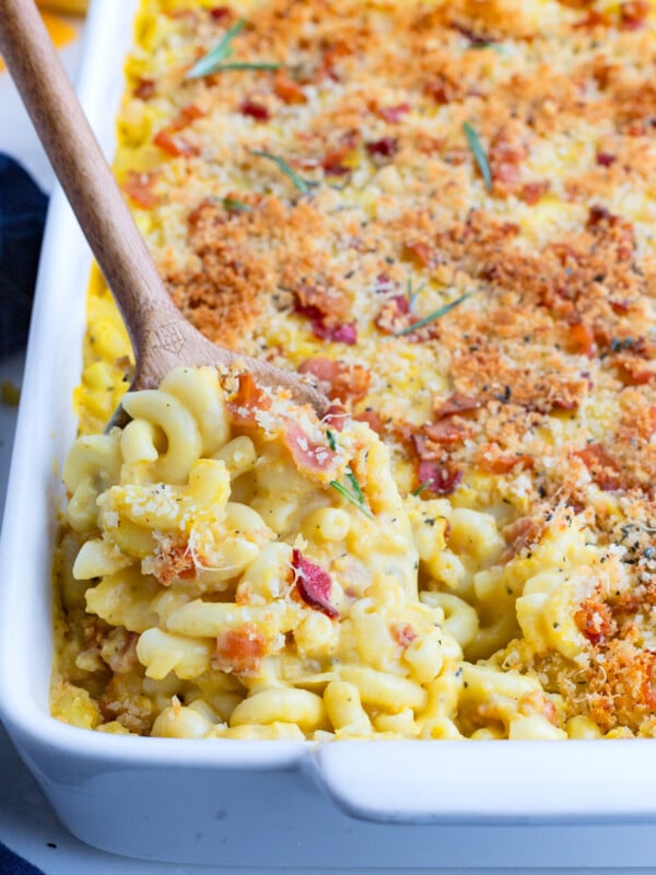 A wooden spoon digs into a pan of mac and cheese with butternut squash.