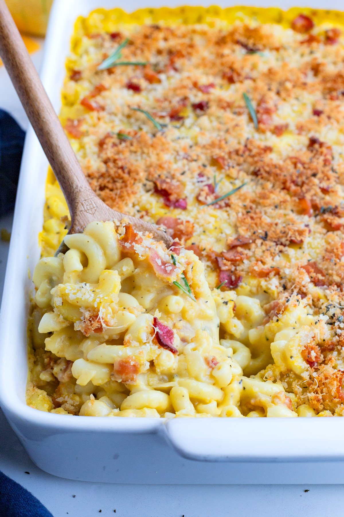 Butternut Squash Mac n Cheese RECIPE in a white casserole dish and a wooden spoon.