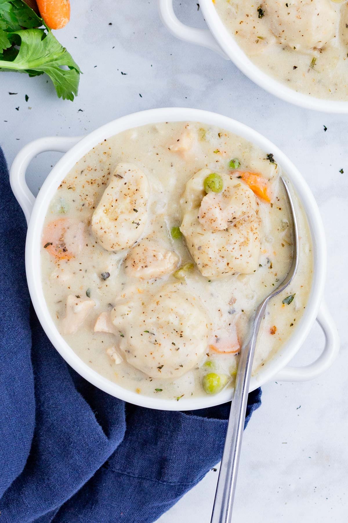 The Best Chicken Dumpling Soup RECIPE served in a white soup bowl and a metal spoon.