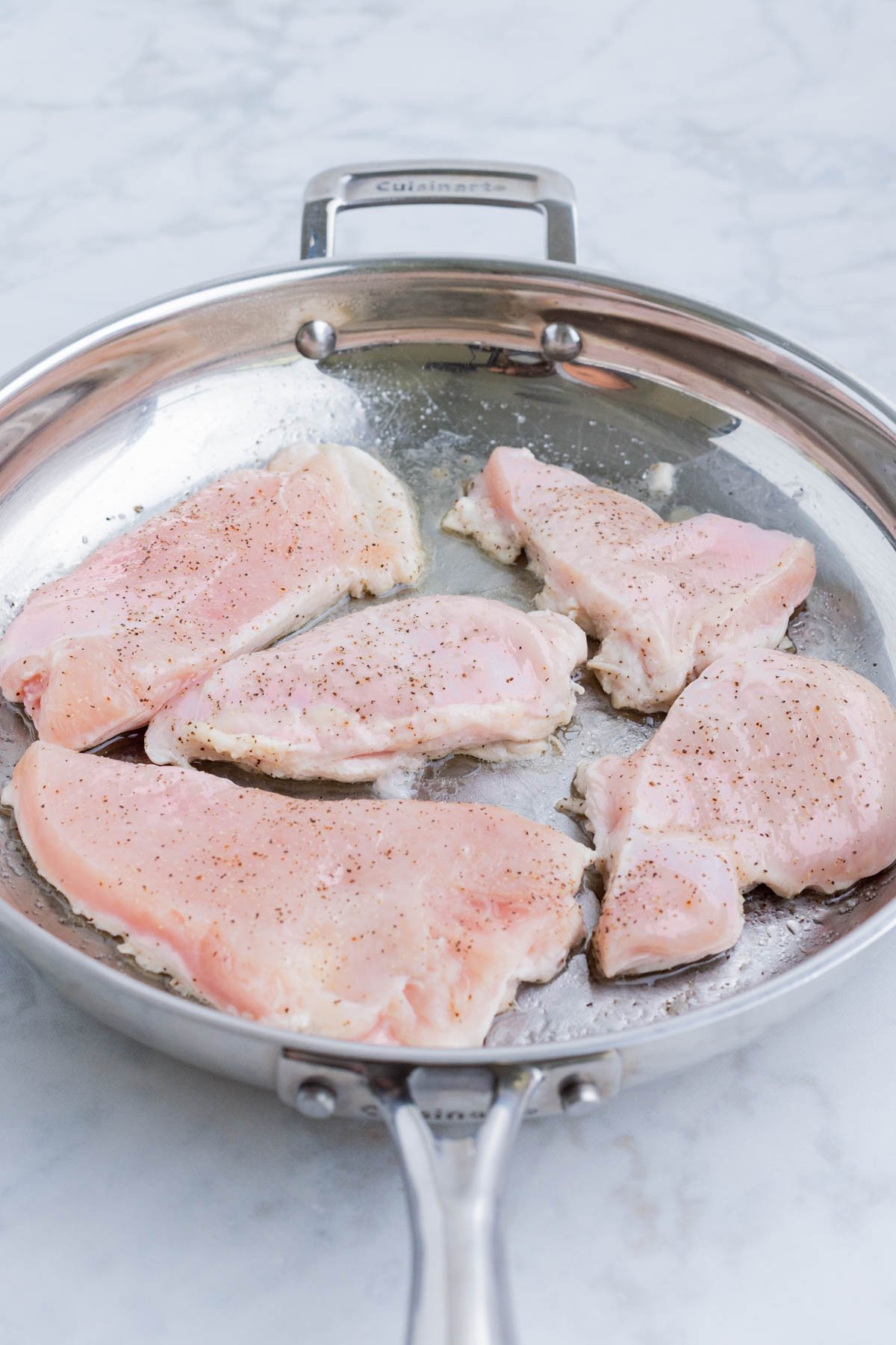Prepared chicken is seared in a skillet.