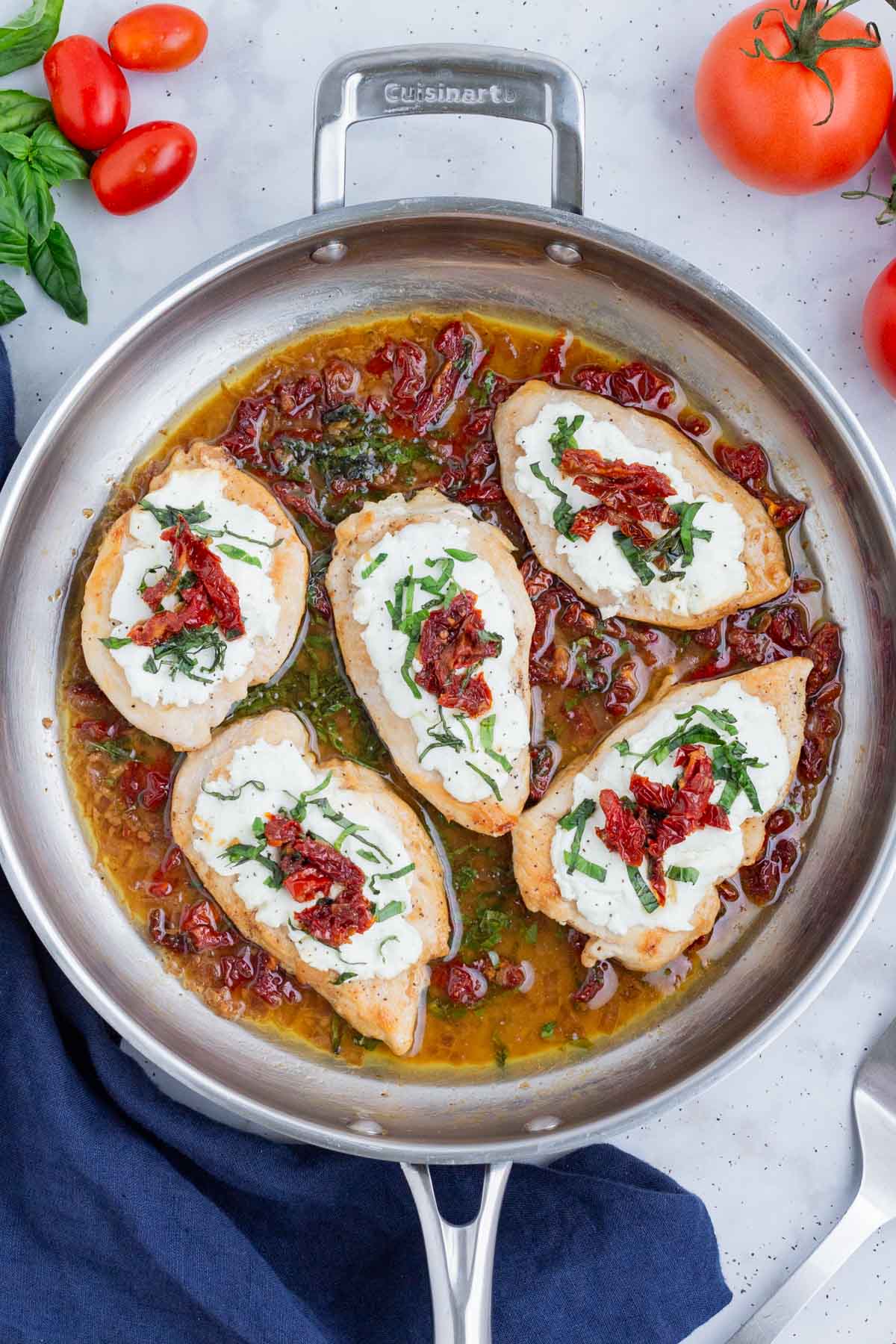 Chicken is cooked with goat cheese, sundried tomatoes, and basil in a skillet.