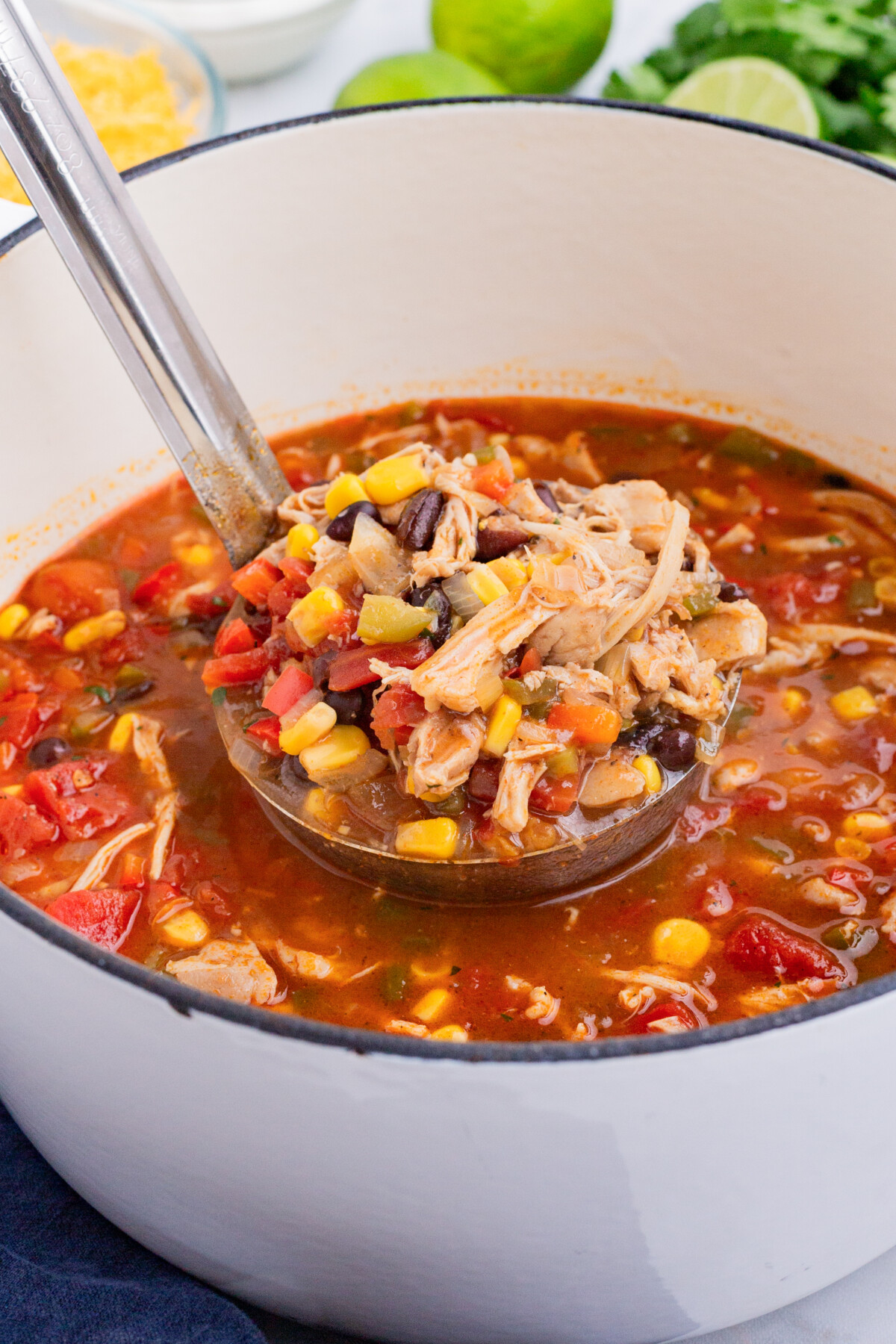 A ladle scoops out chicken enchilada soup from a white Dutch oven.
