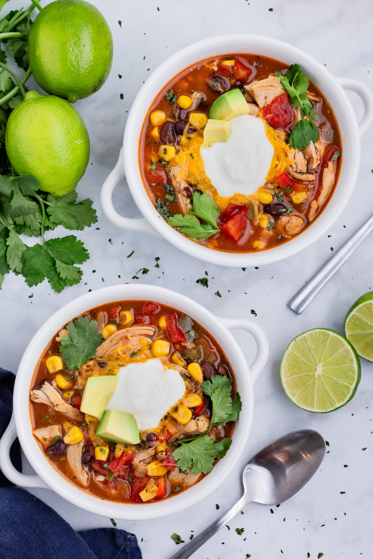 Two white soup bowls are full of a chicken enchilada soup recipe.