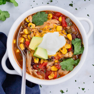 A white bowl is full of chicken enchilada soup and topped with sour cream and avocado.