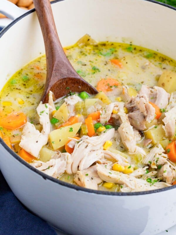 Chicken pot pie soup recipe is in a white Dutch oven with a wooden spoon.