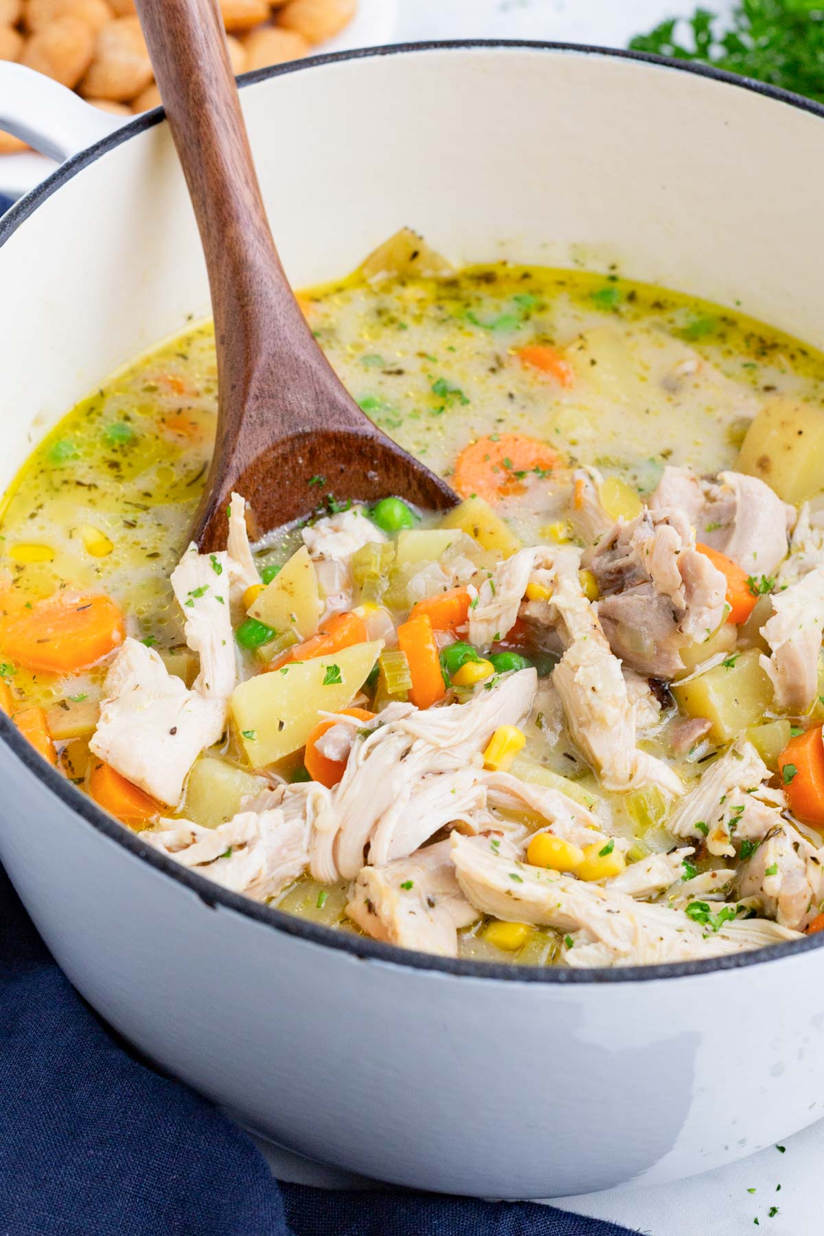 Chicken pot pie soup recipe is in a white Dutch oven with a wooden spoon.