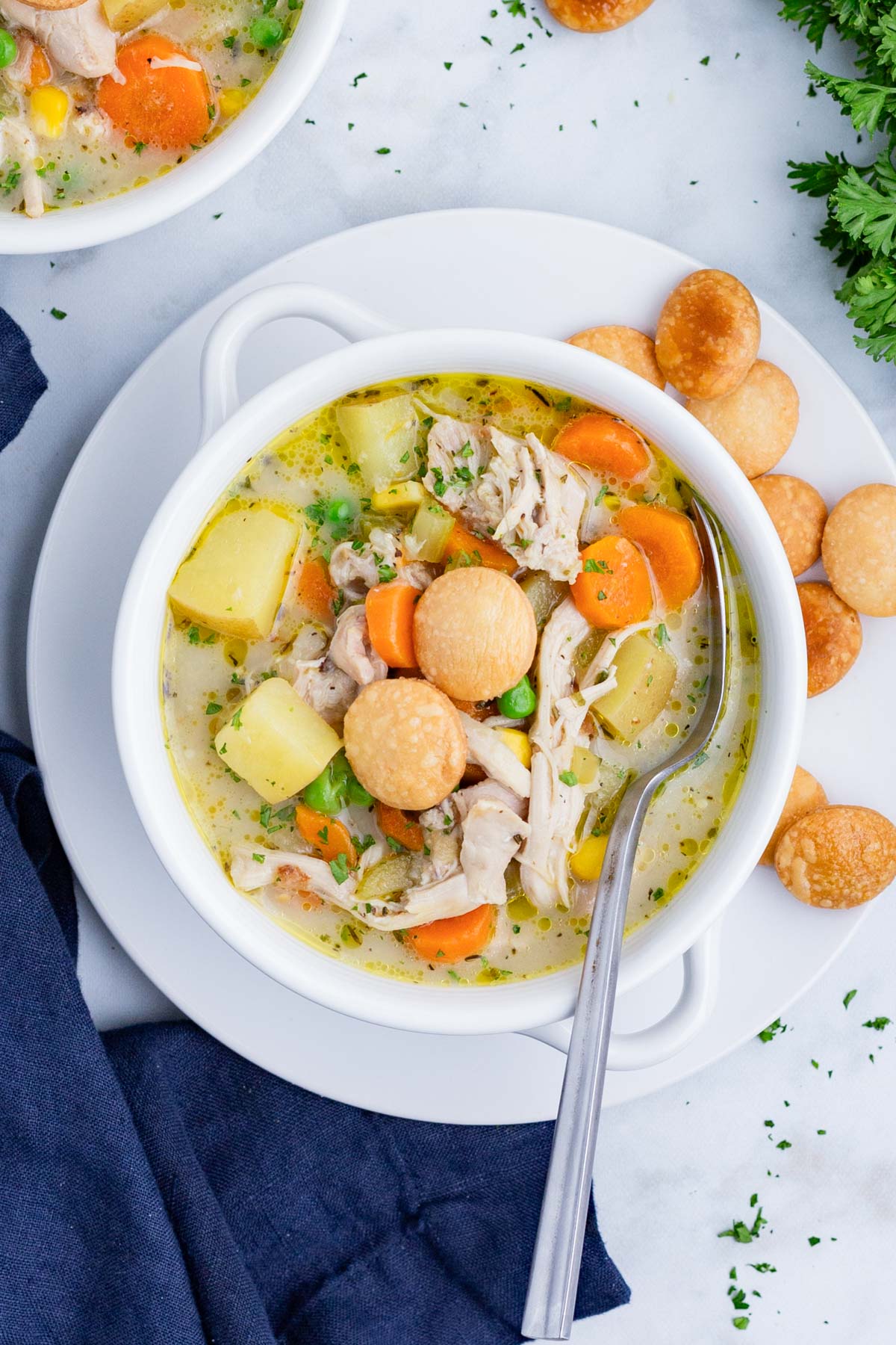 A bowl full of Chicken Pot Pie Soup is on a plate with pie crust crackers.