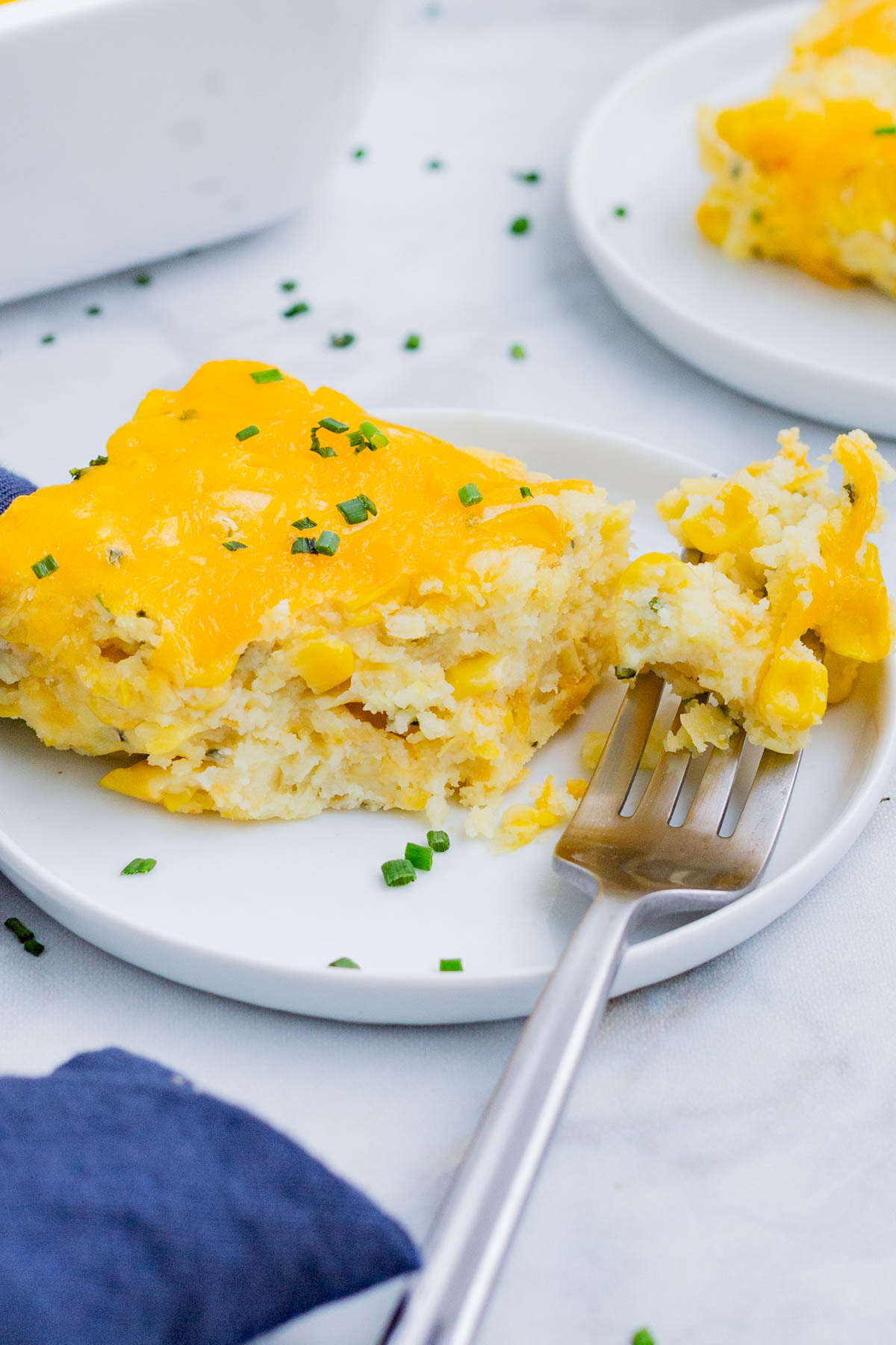 A fork digs into a serving of corn casserole on a white plate.