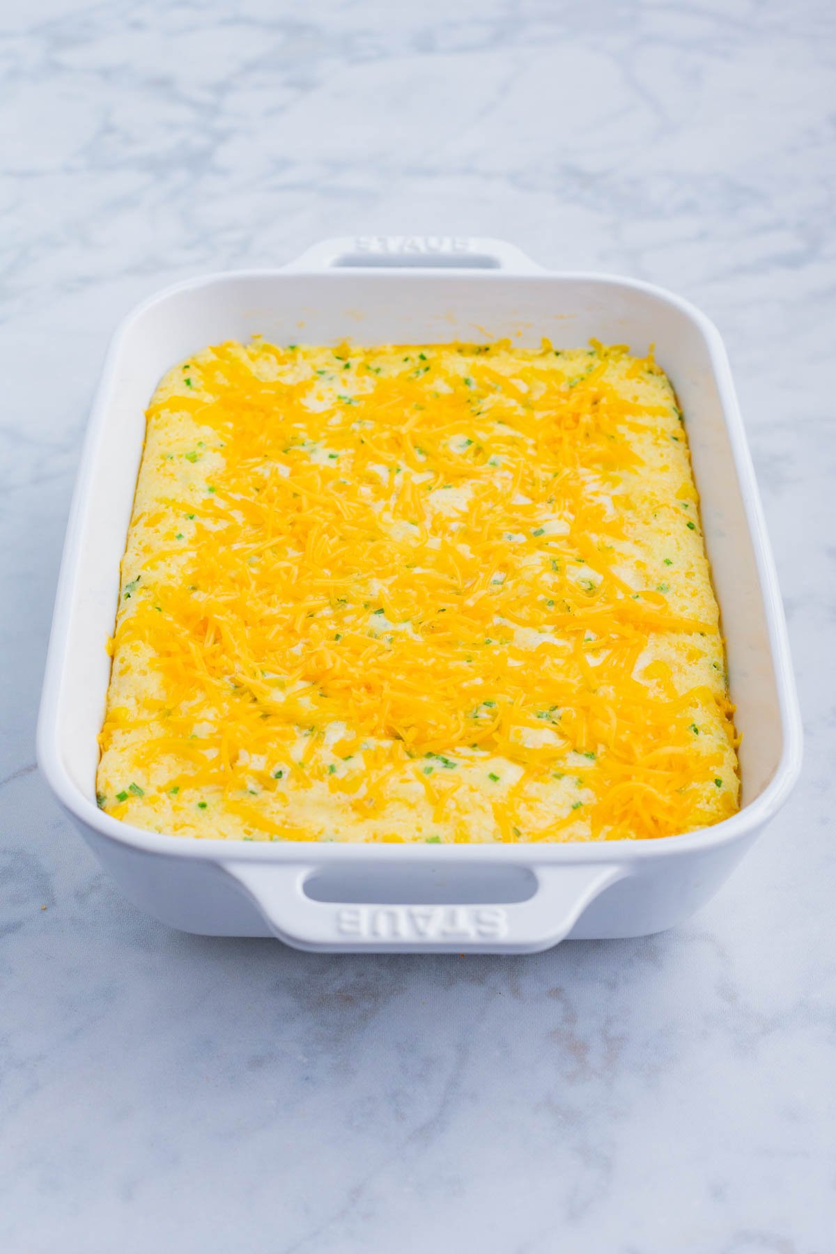 Corn souffle is topped with shredded cheese before baking.