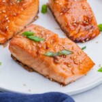 Three salmon fillets cooked in a honey sriracha sauce are served on a white plate.