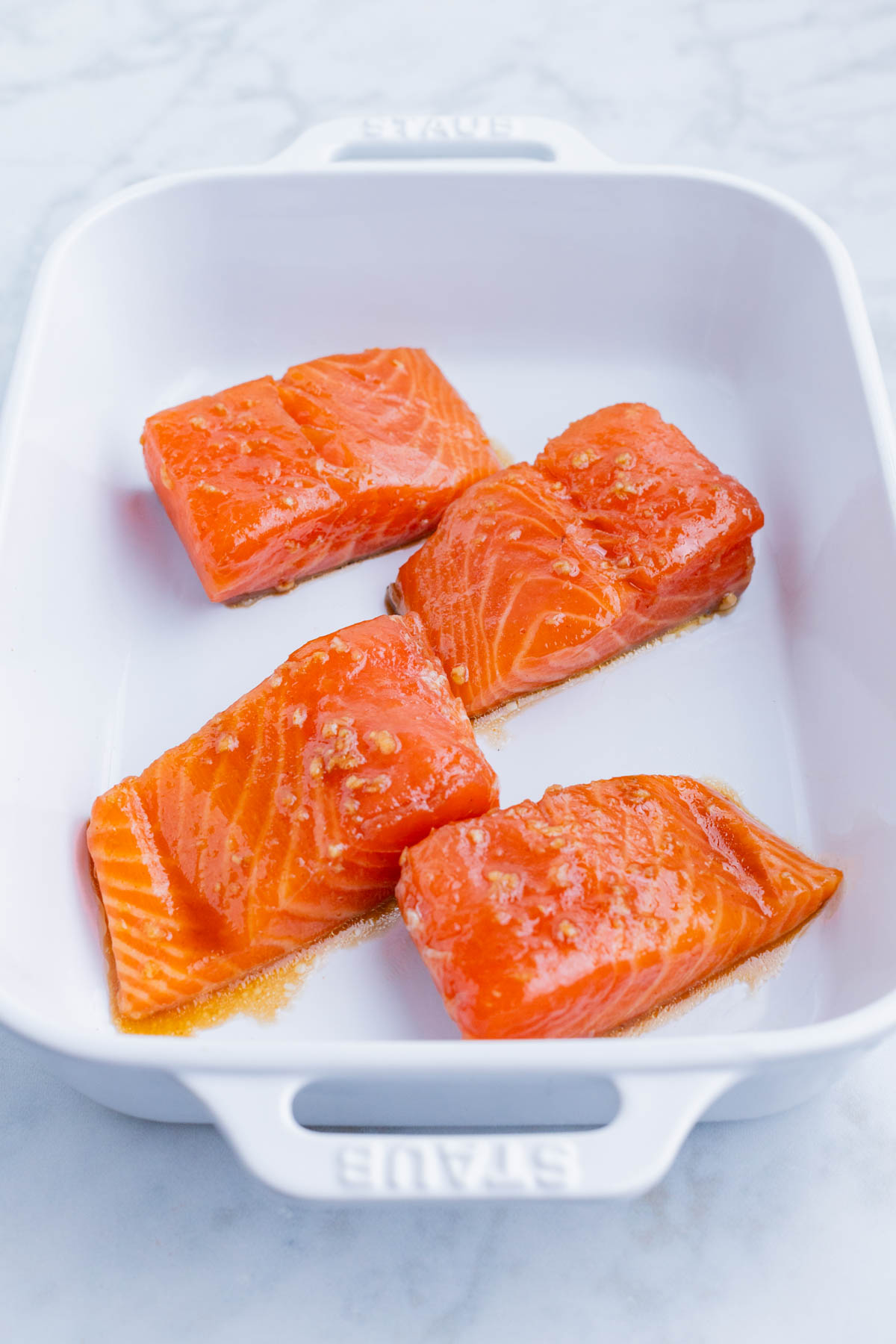 Marinated salmon fillets are baked in a casserole dish.