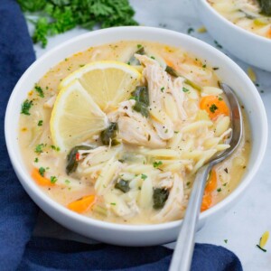 A white Dutch oven is full of Lemon Chicken Orzo Soup with a wooden spoon.