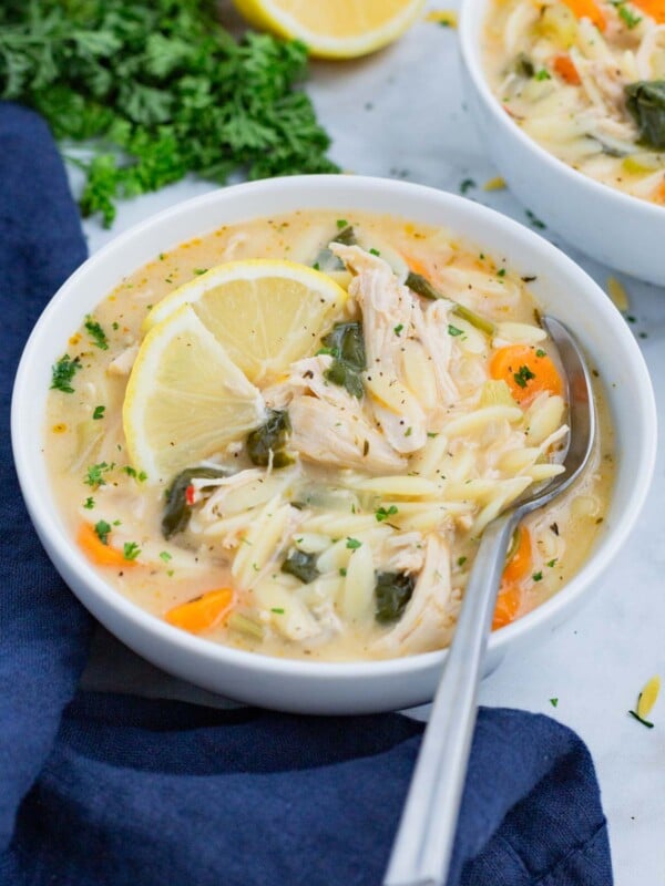 A white Dutch oven is full of Lemon Chicken Orzo Soup with a wooden spoon.
