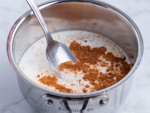 Oats, milk, and syrup, and cinnamon are added to a saucepan for a maple brown sugar oatmeal recipe.