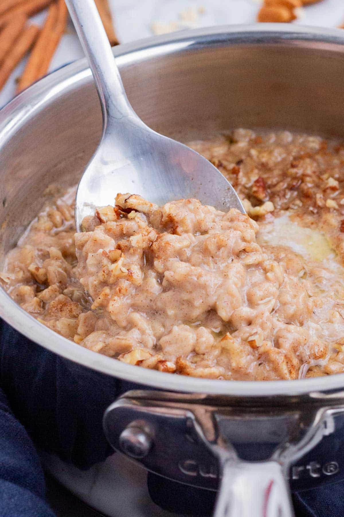 A metal spoon stirs oatmeal in a pot.