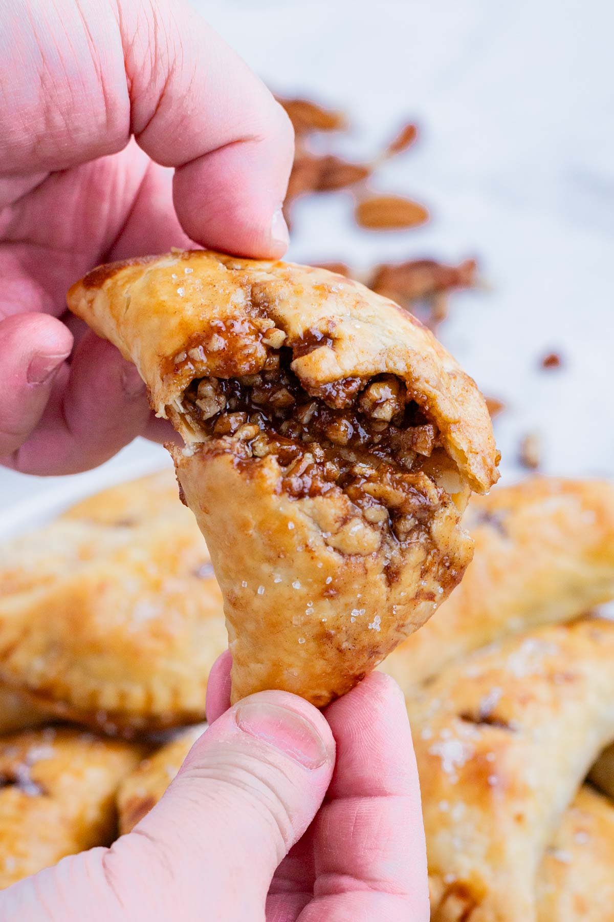 A hand rips open a pecan hand pie to show the filling.