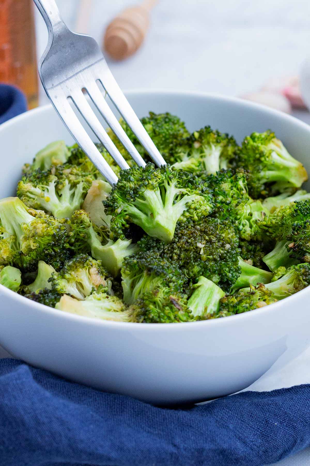 A fork digs into a bowl full of broccoli that was roasted in the oven.