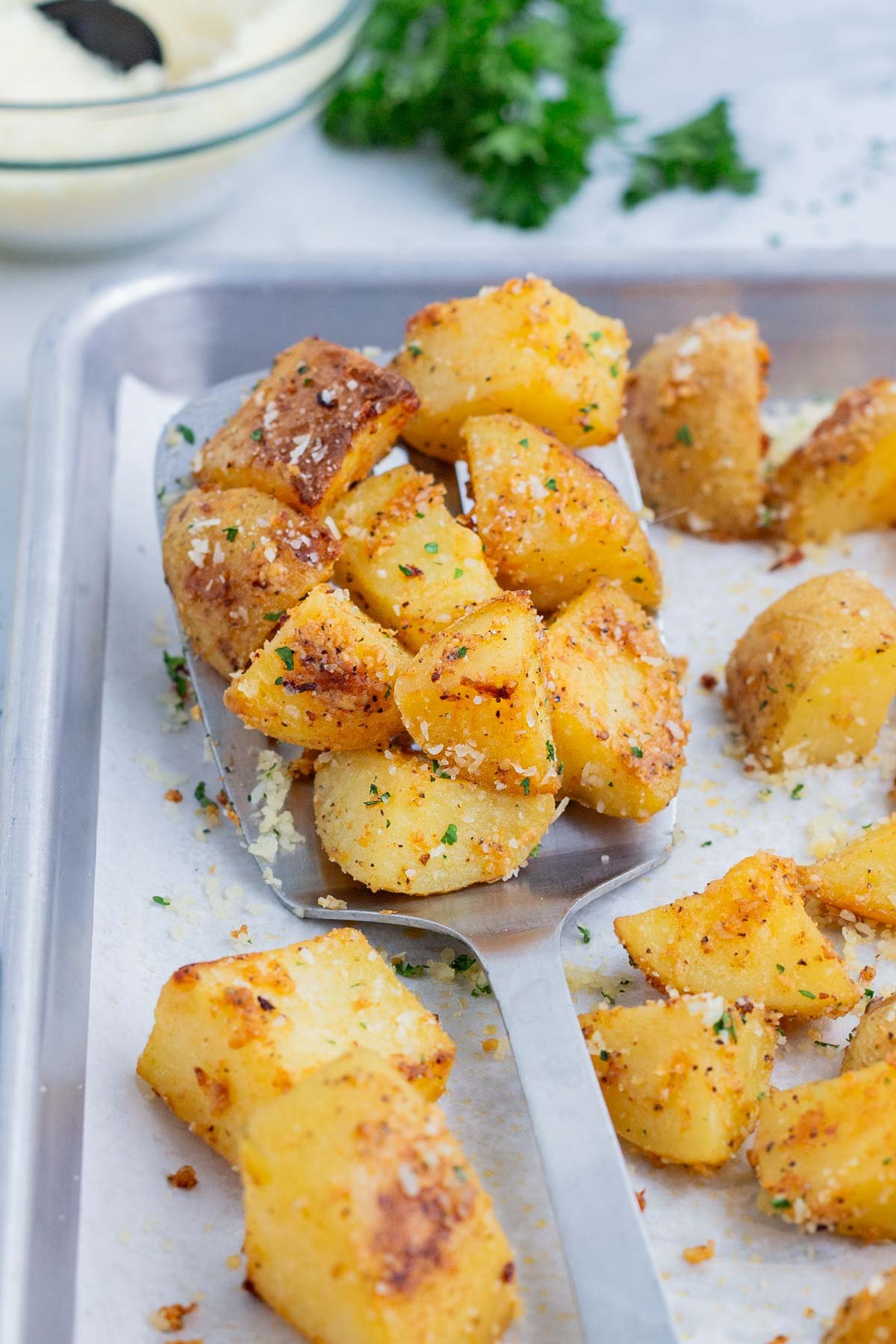 A metal spatula scoops roasted potatoes from the baking sheet.