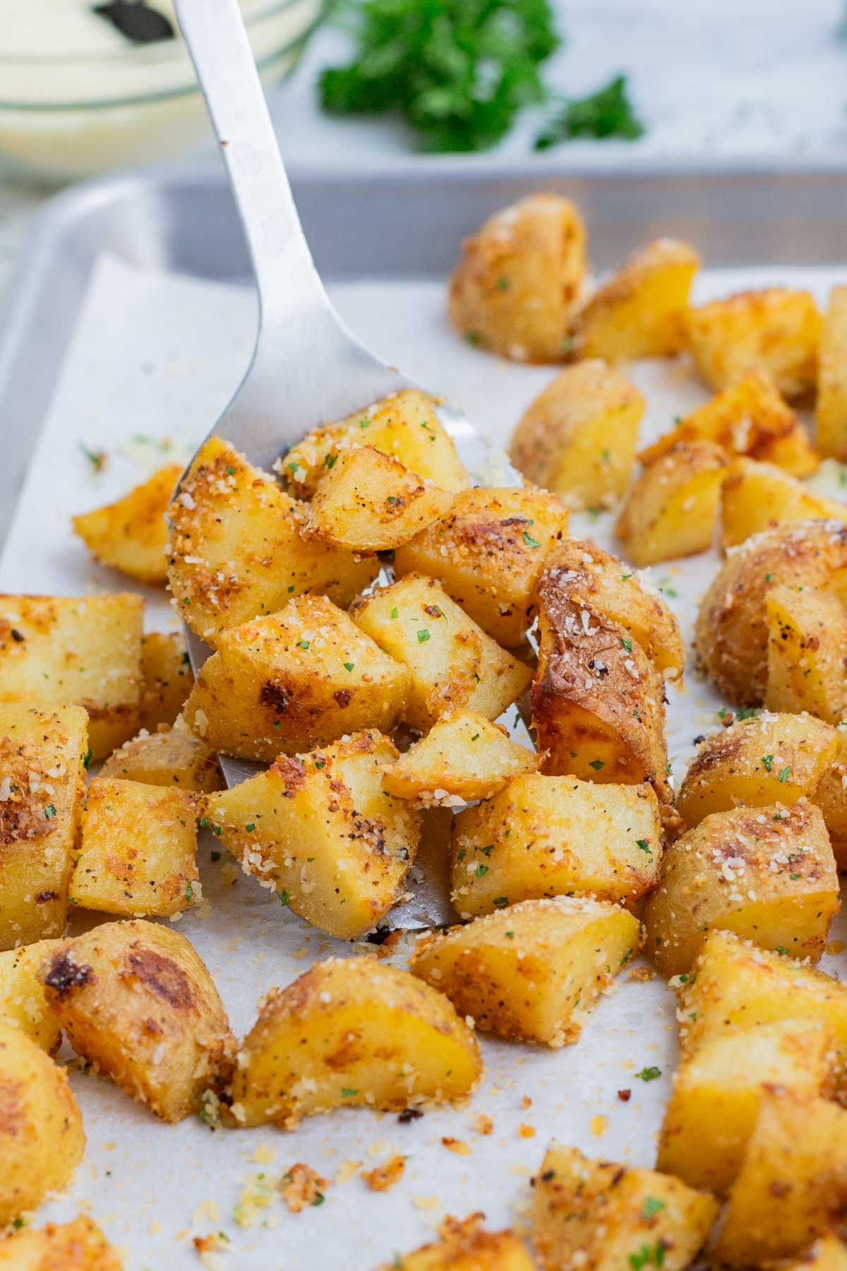 A metal spatula scoops roasted potatoes from the baking sheet.