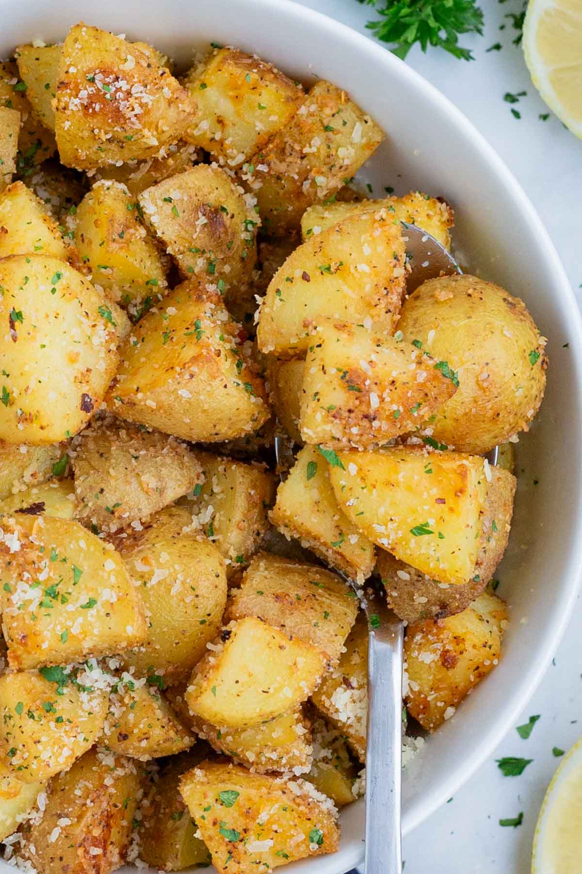 A spoon is used to scoop up roasted potatoes from a white bowl.