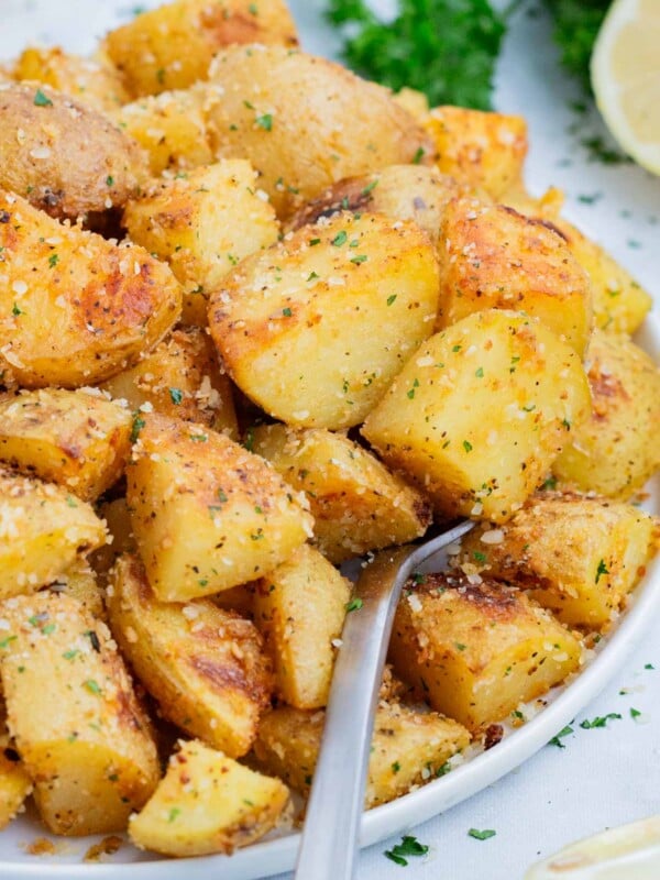 A spoon is used to scoop up roasted potatoes from a white bowl.