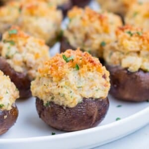 A round, white plate is full of stuffed mushrooms.