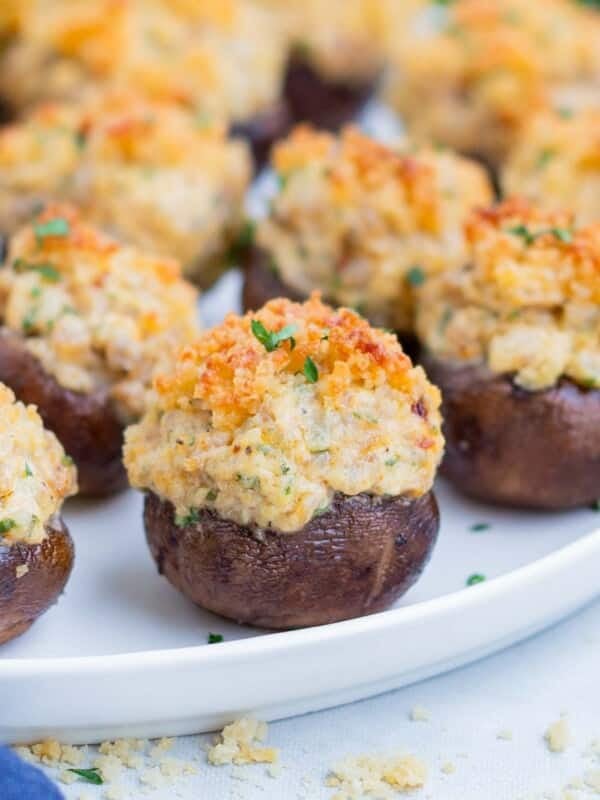 A round, white plate is full of stuffed mushrooms.