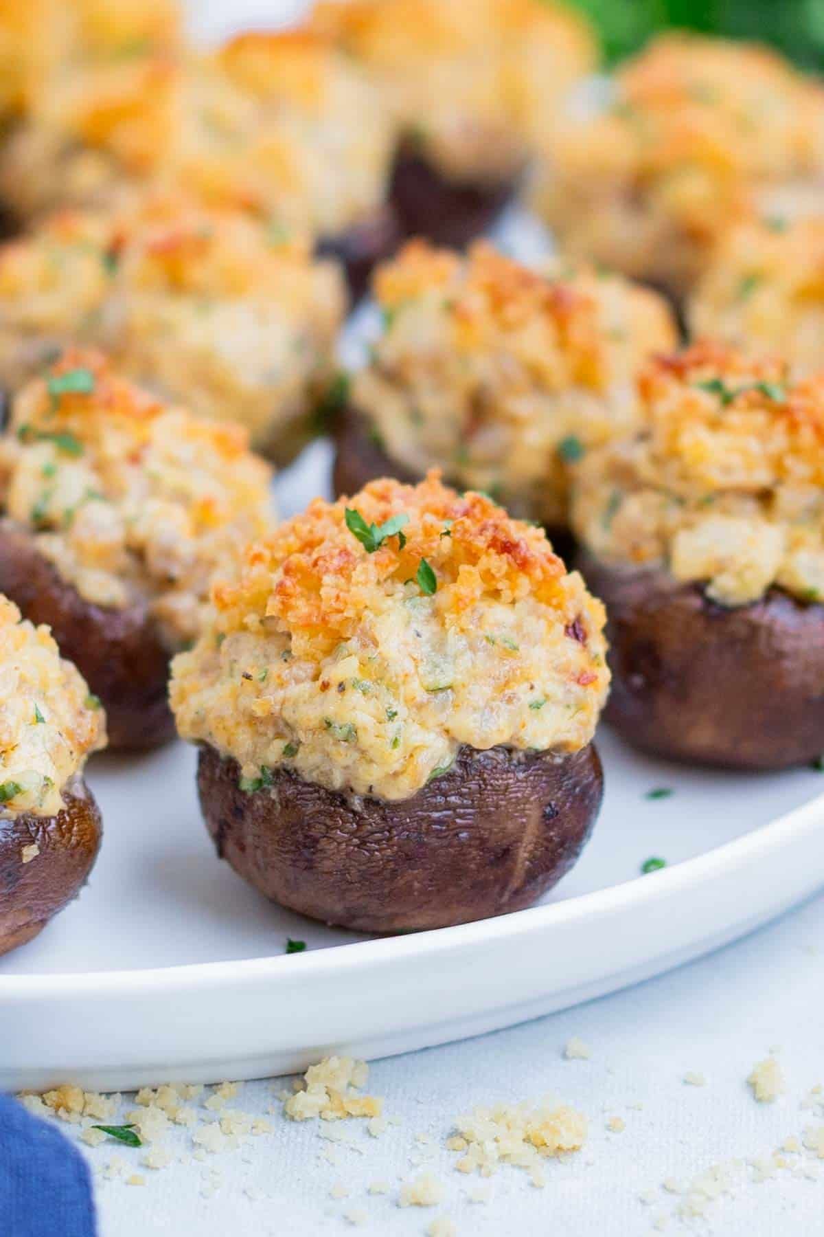 A round, white plate is full of stuffed mushrooms.