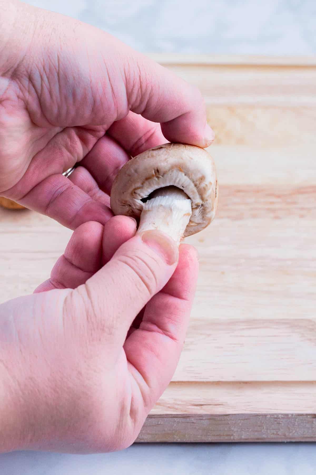 A hand removes the stem of a mushroom.