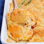 A metal spoon is used to scoop sweet potato au gratin from a casserole dish.