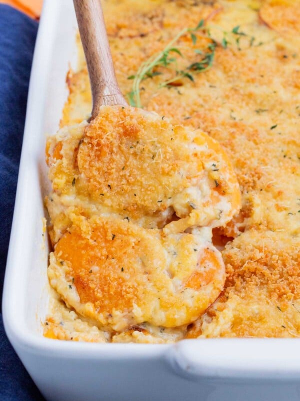 A metal spoon is used to scoop sweet potato au gratin from a casserole dish.