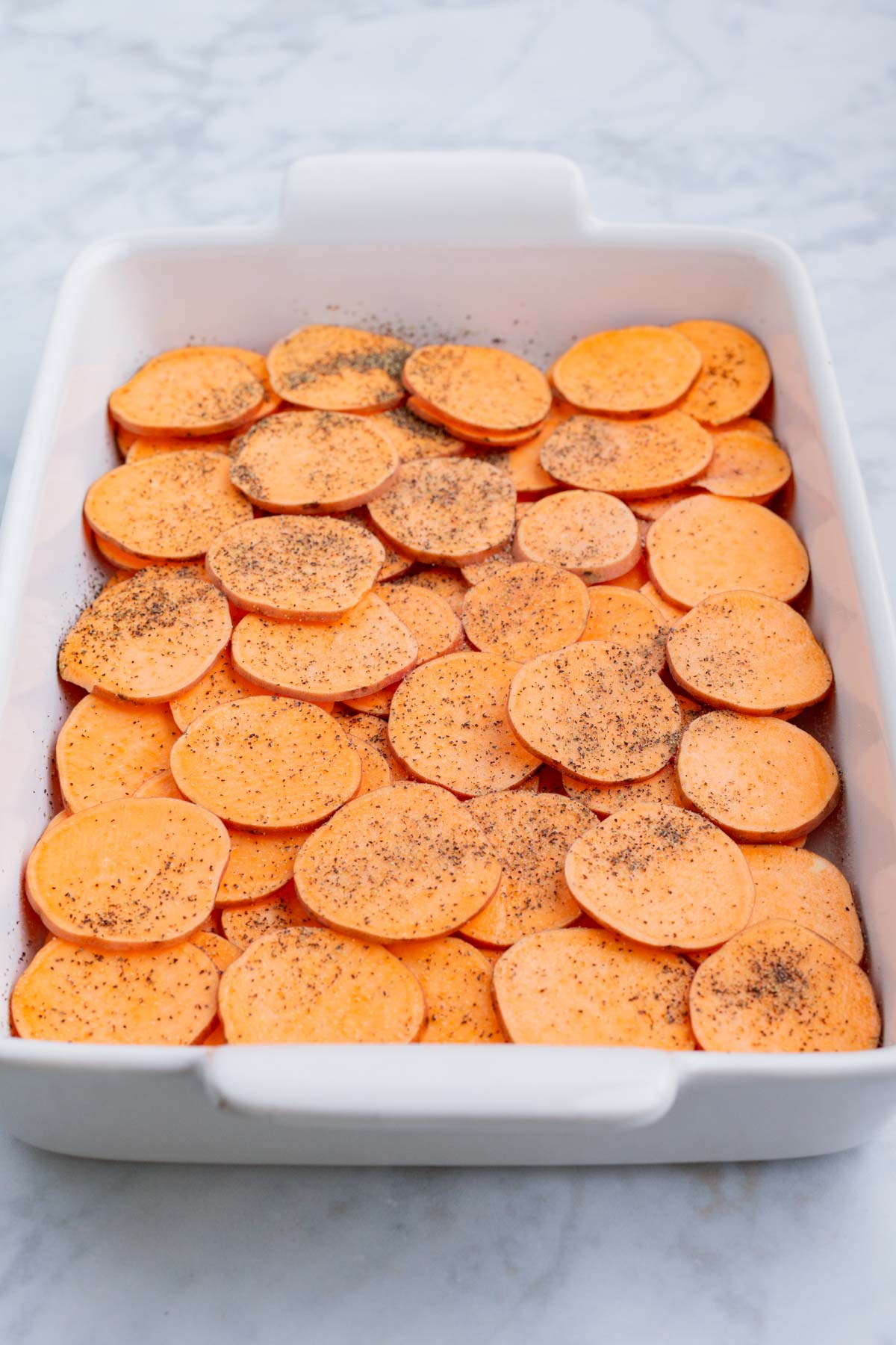 Sliced sweet potatoes are spread across a casserole pan.