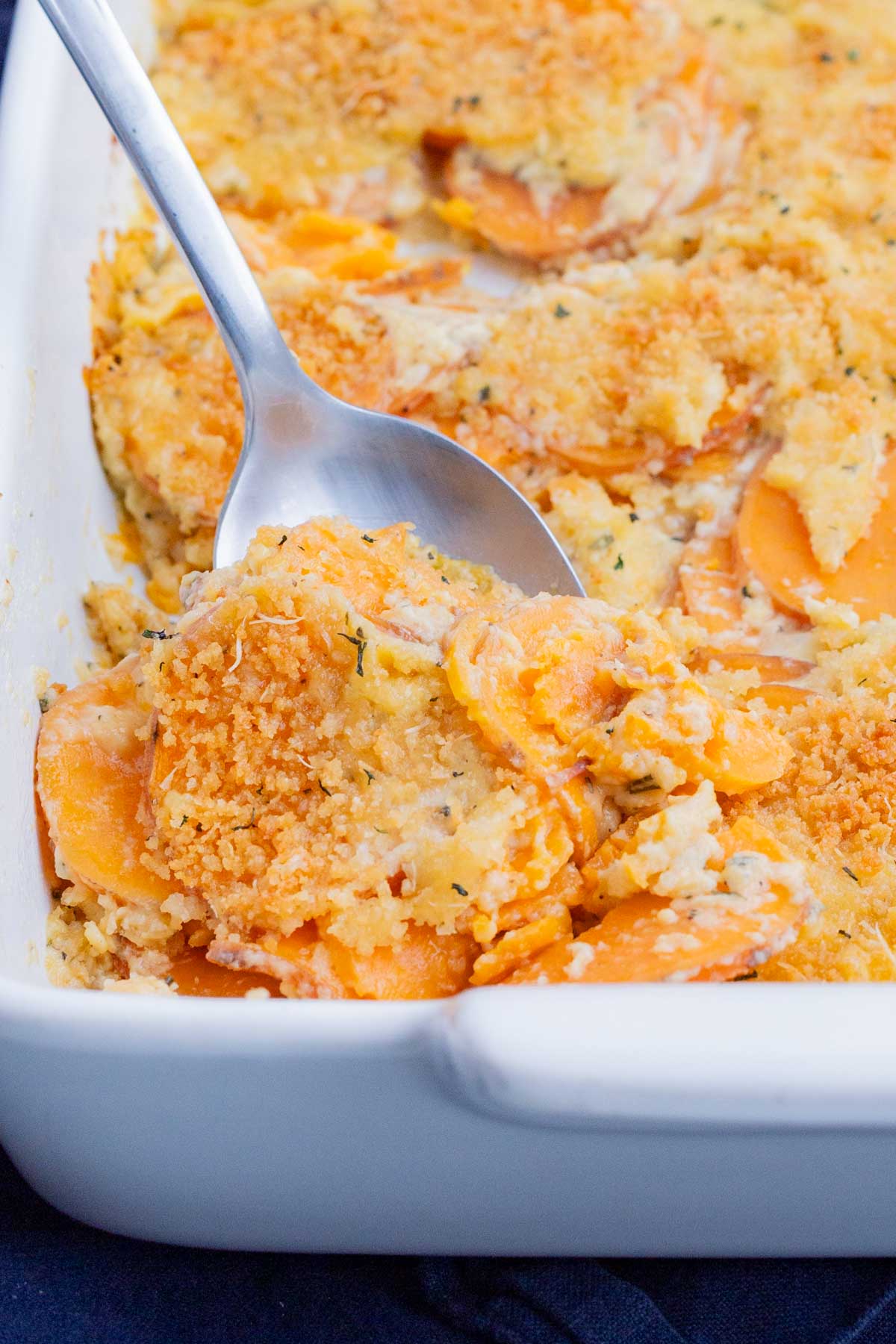A metal spoon is used to scoop sweet potato au gratin from a casserole dish.