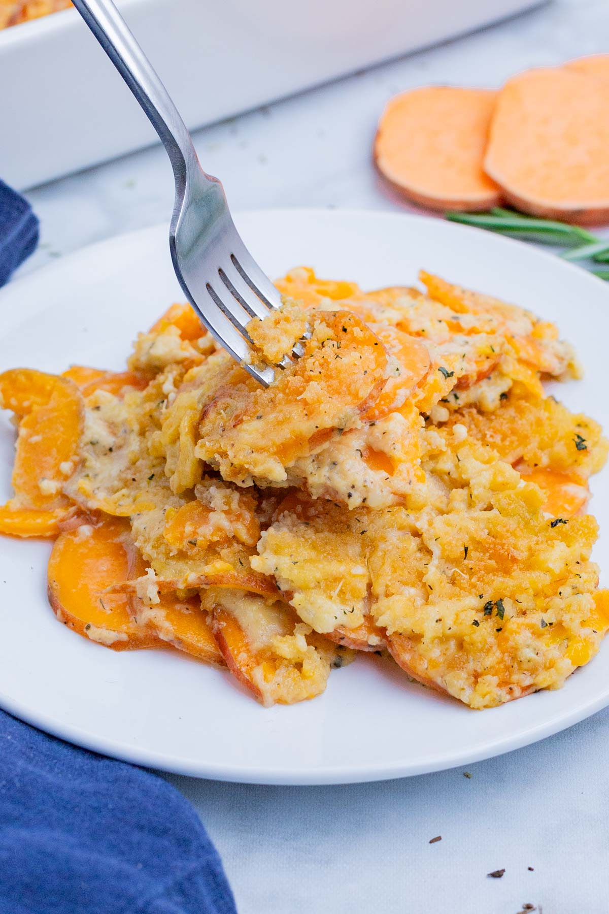 A fork digs into a big serving of sweet potato au gratin on a white plate.