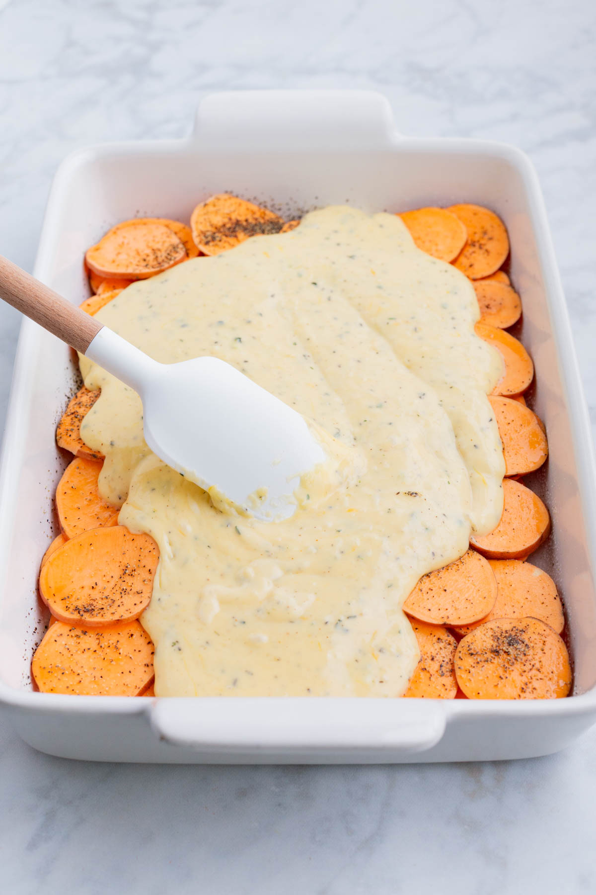 The cheese sauce is spread across the sliced sweet potatoes.