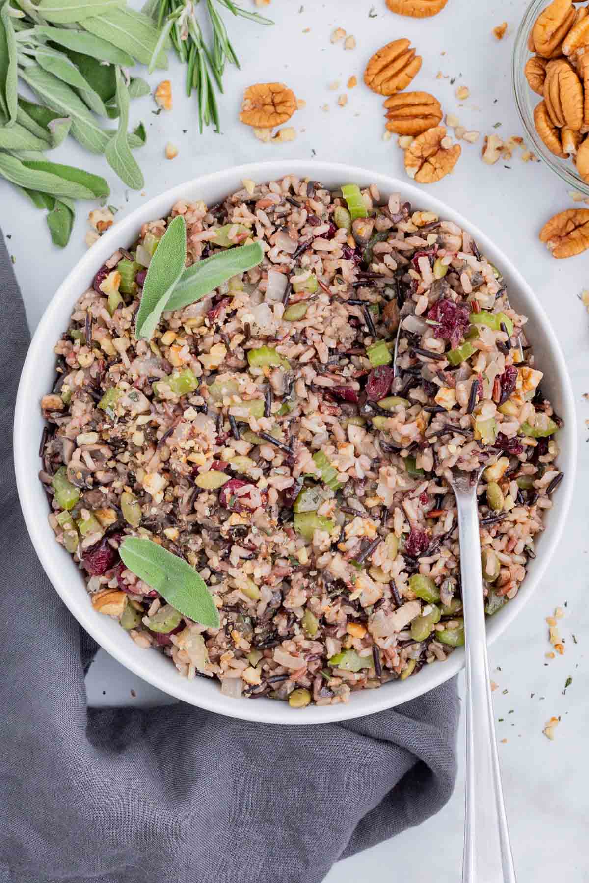 Wild Rice Stuffing with Cranberries RECIPE served in a white bowl, with a spoon, and fresh sage.