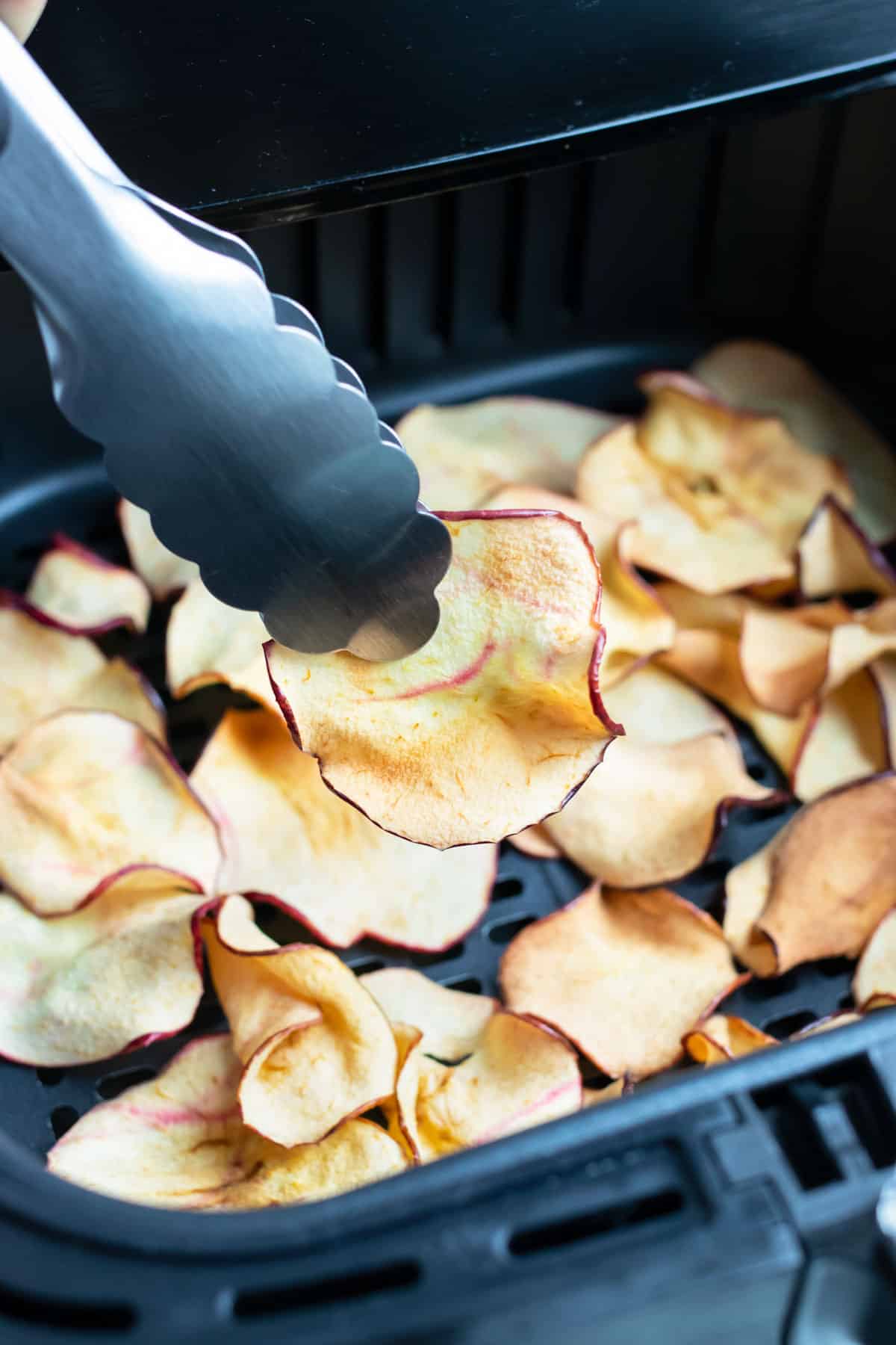 Tongs are used to remove the air fryer apple chips.