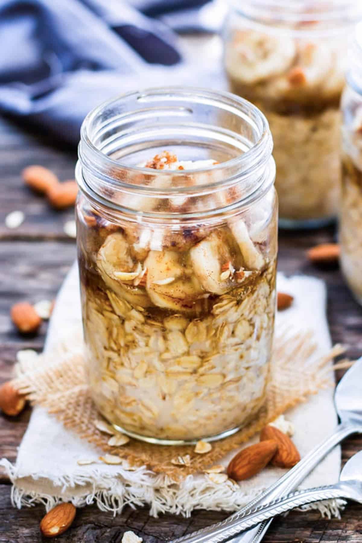 Three jars filled with Almond Butter Banana Overnight Oats on a table for breakfast.