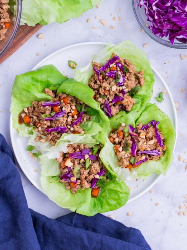 Four Thai chicken lettuce wraps are served on a white plate.