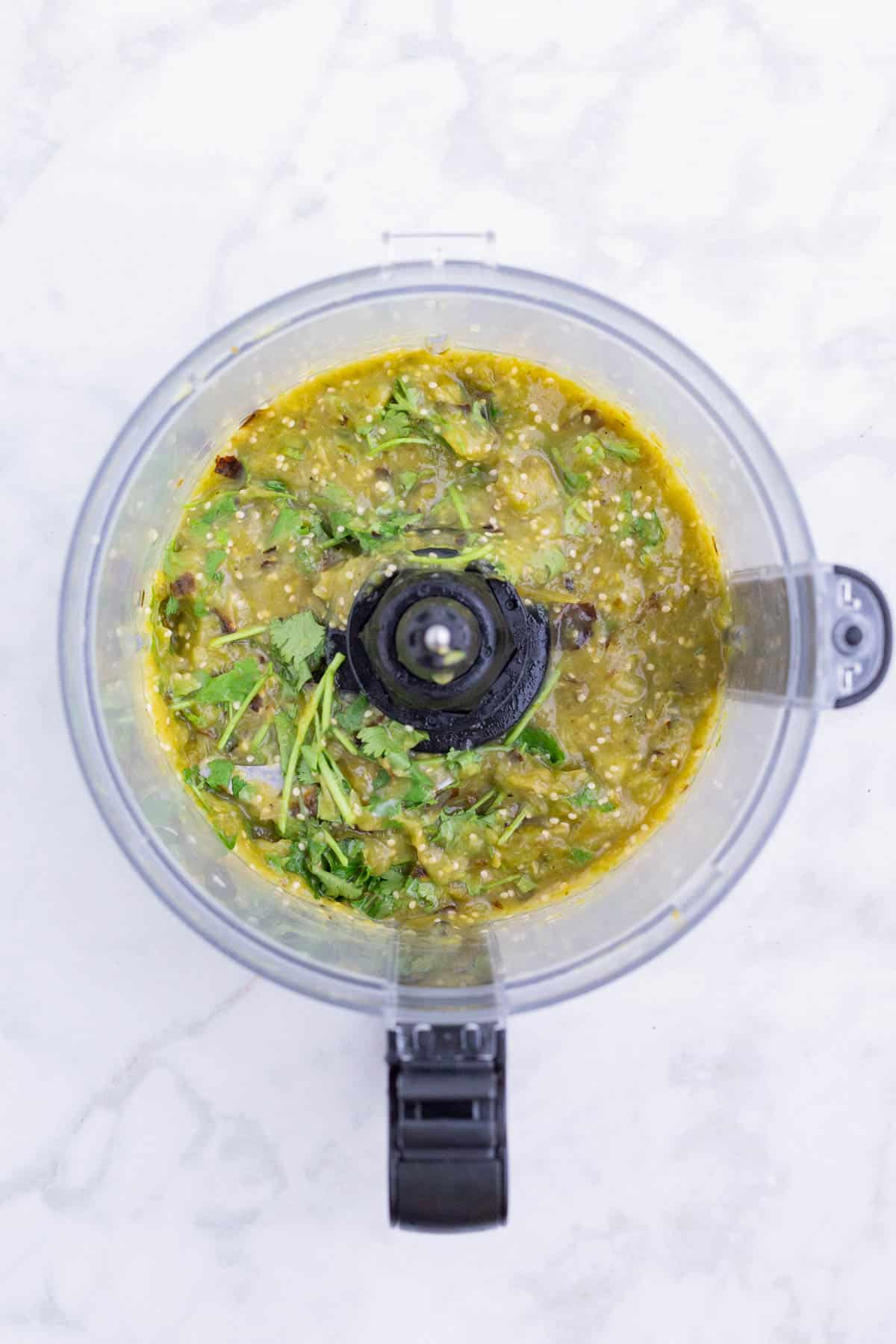 Tomatillos and jalapeno are processed in a food processor.
