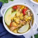 A white bowl full of green chile chicken soup is served with toppings.