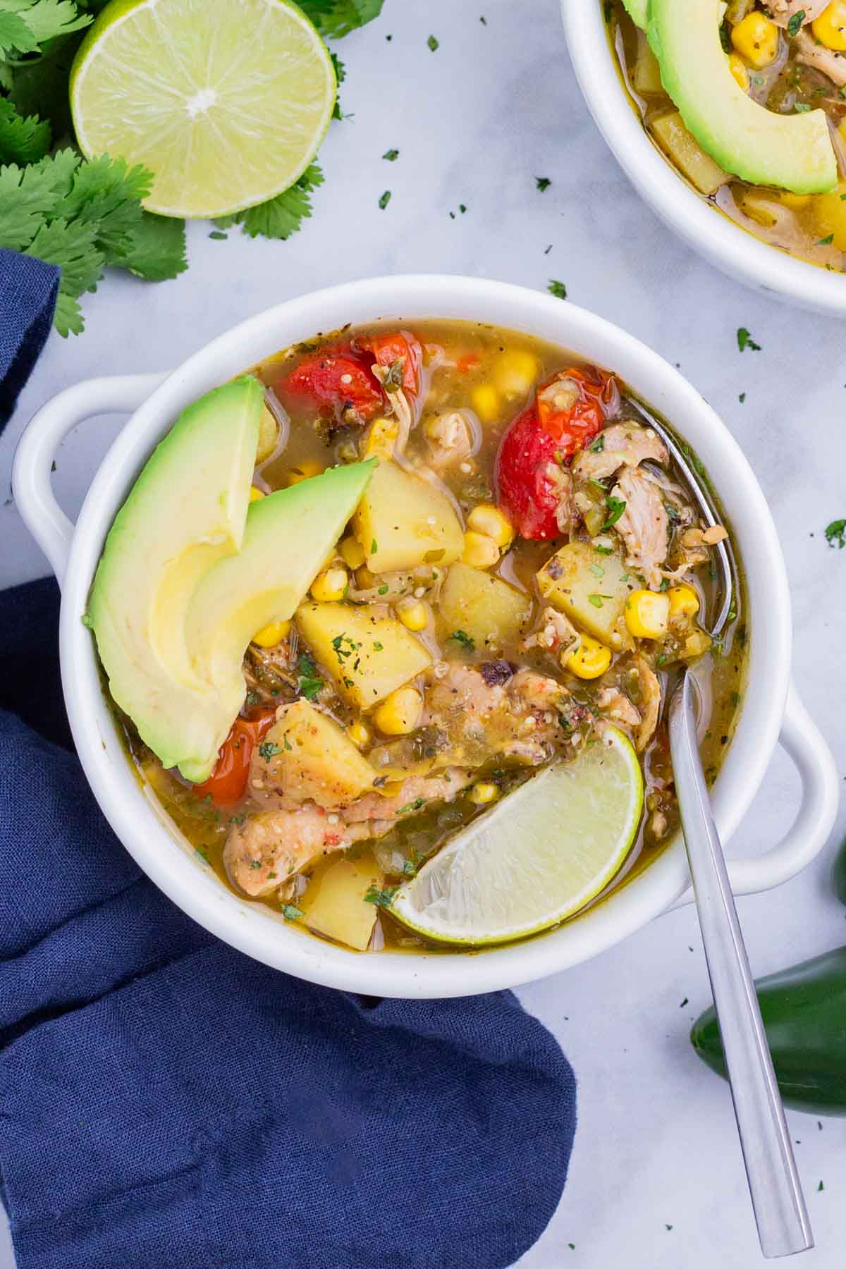 A white bowl full of green chicken chili soup is served with toppings.