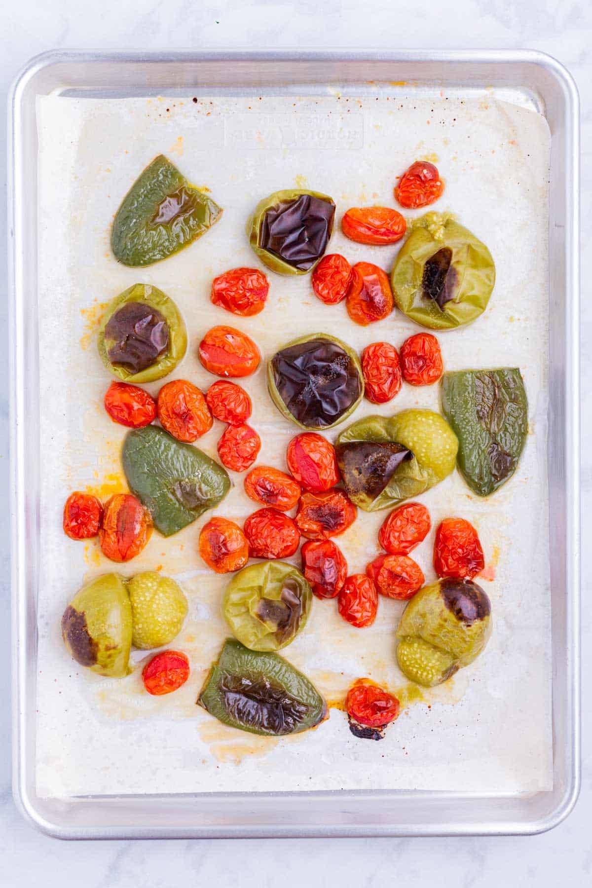 Peppers, tomatillos, and tomatoes are roasted on a pan.