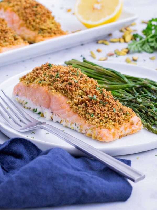 A piece of pistachio-crusted salmon is served on a white plate with green beans.