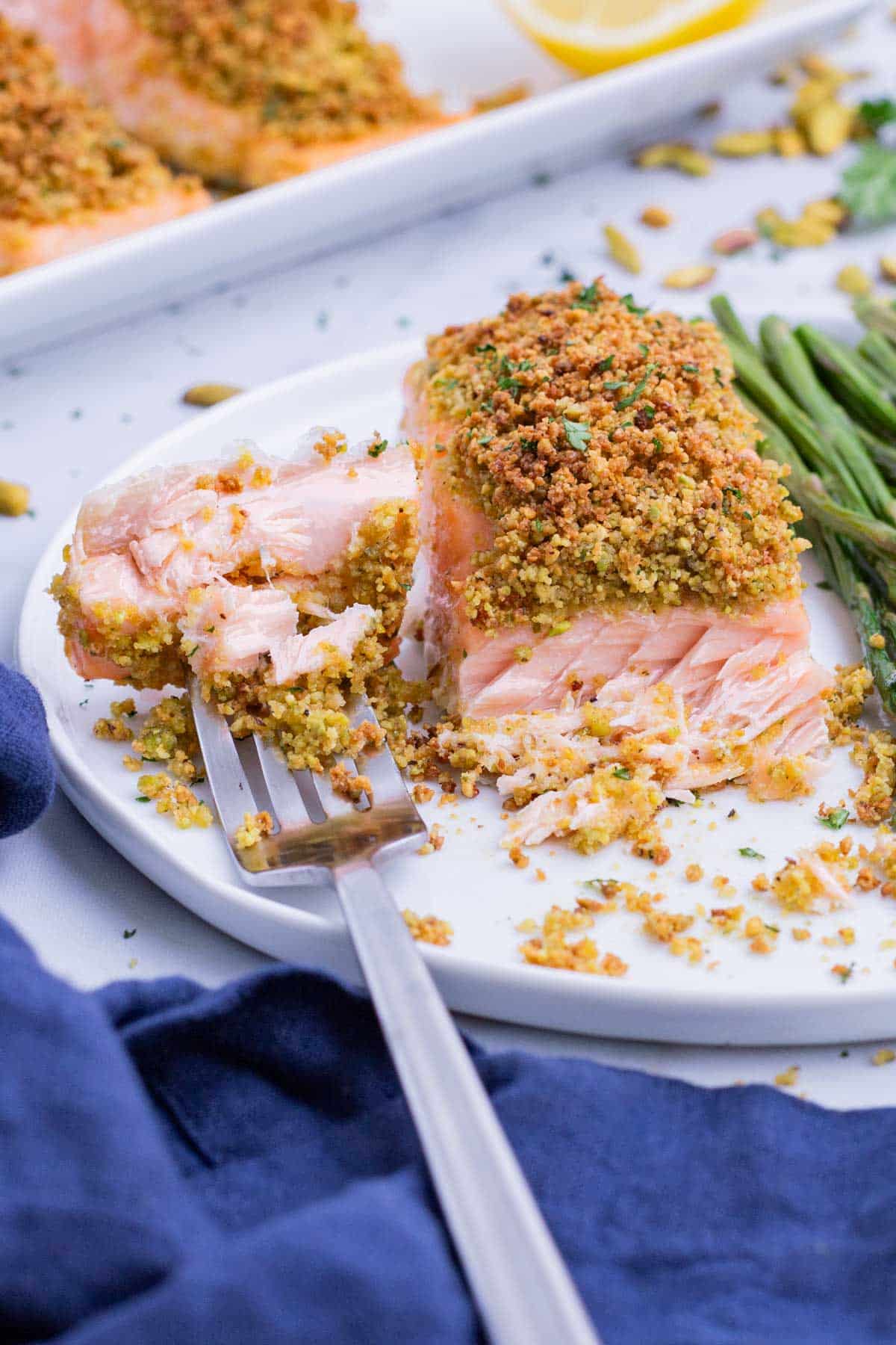 A fork digs into a filet of salmon with a pistachio topping.