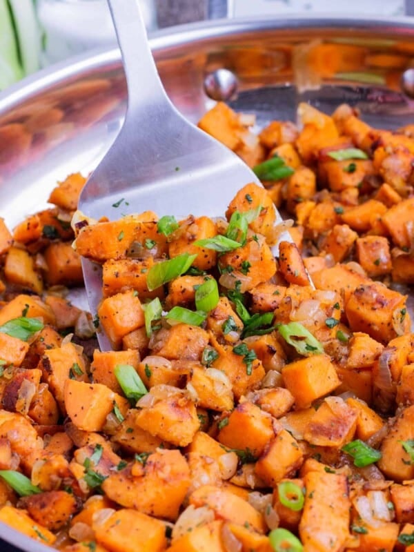 A metal spatula stirs green onions and cilantro into the sauteed sweet potatoes.