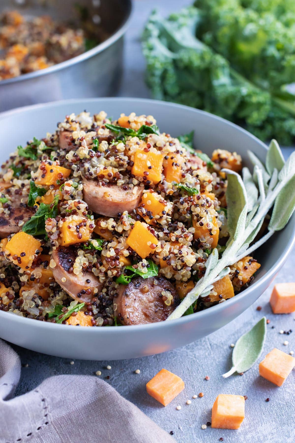 A grey bowl full of a quinoa, sausage, and sweet potato recipe with sage.