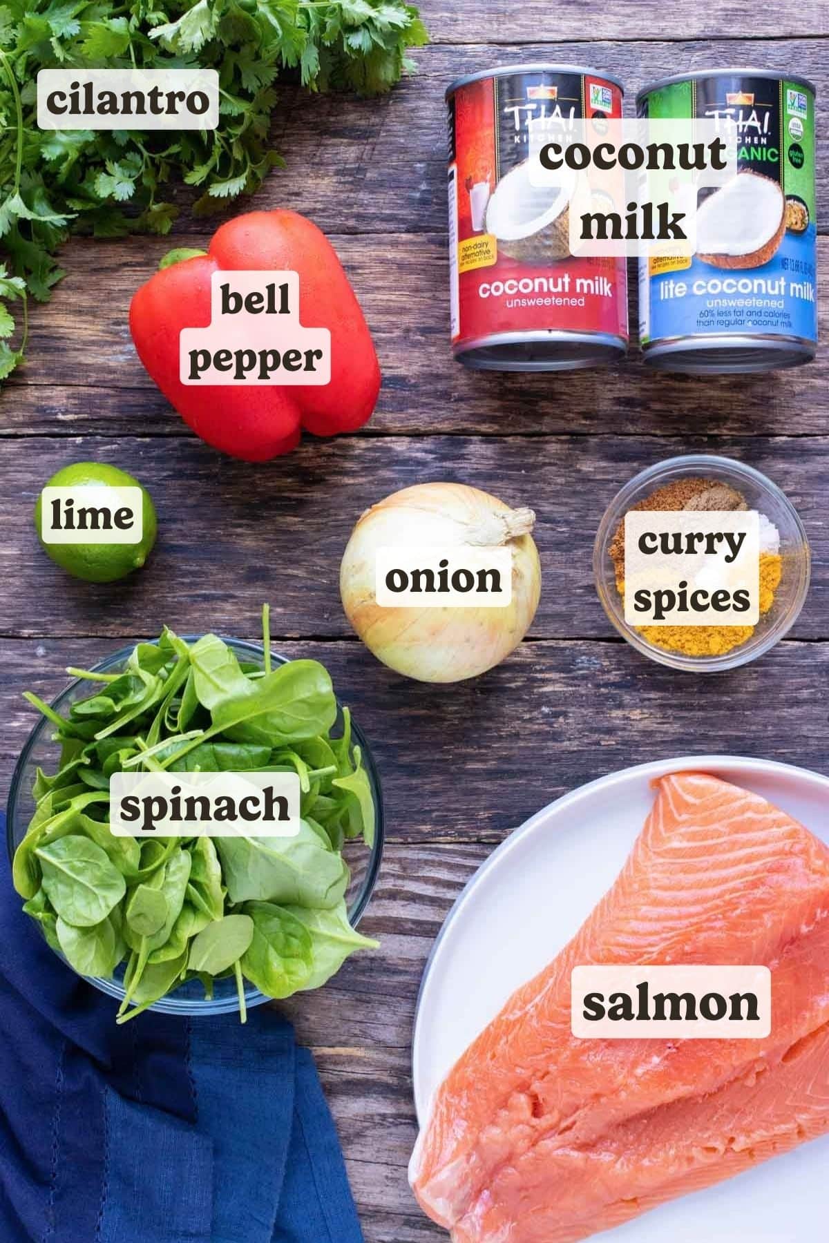 Coconut milk, salmon, spinach, curry spices, and lime on a wooden board as the ingredients for a salmon curry recipe.