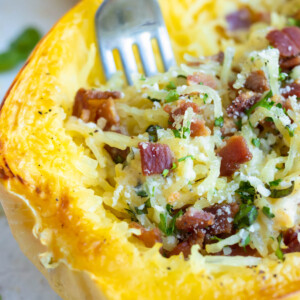 A fork digging into a Spaghetti Squash Carbonara studded with bacon.
