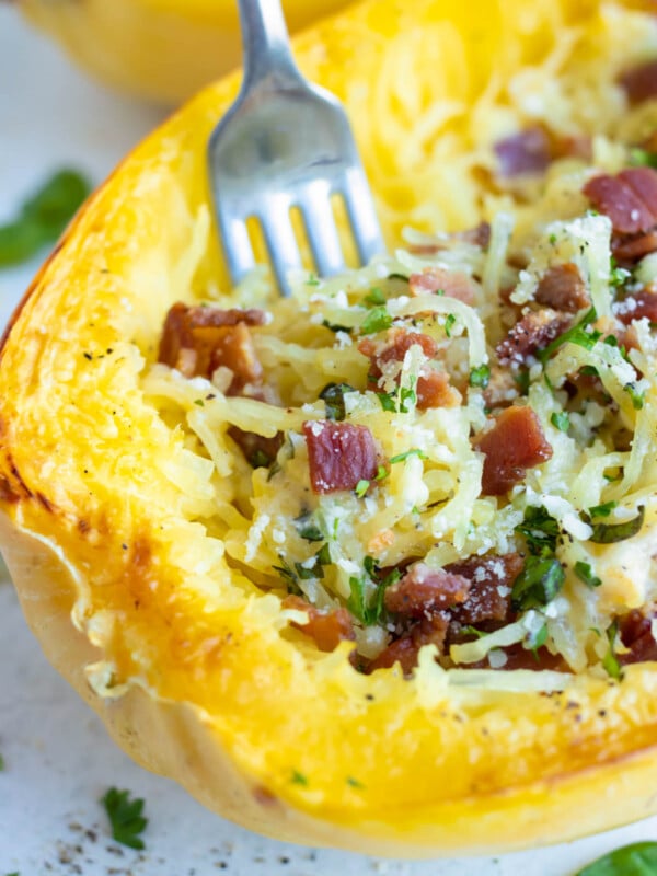 A fork digging into a Spaghetti Squash Carbonara studded with bacon.